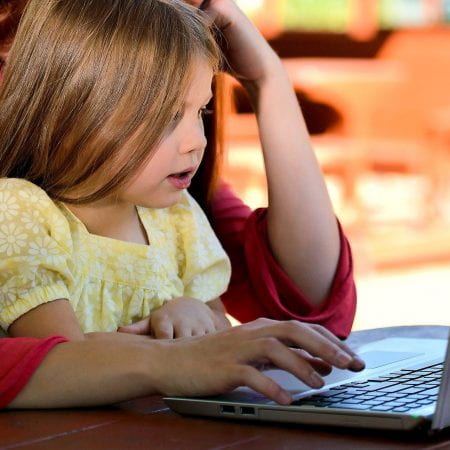A young girl sitting on a womans lap looking at a laptop
