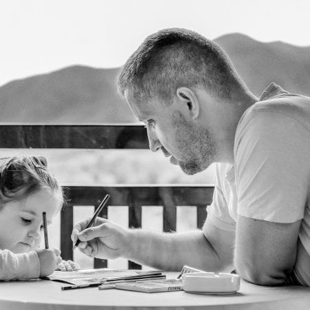 This picture is in blackboard and white. it shows a girl and a man writing on a document. There is a view of the sea and mountains in the background.